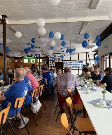 Gesellige Veranstaltung in einem Raum mit blauen und weißen Luftballons und festlich gedeckten Tischen.